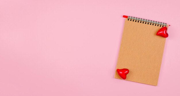 Leeres Notizbuch mit Kraftpapier auf rosafarbenem Hintergrund mit Herzen Das Konzept des Valentinstag-Muttertags-Mockup für Glückwünsche oder Einladungen