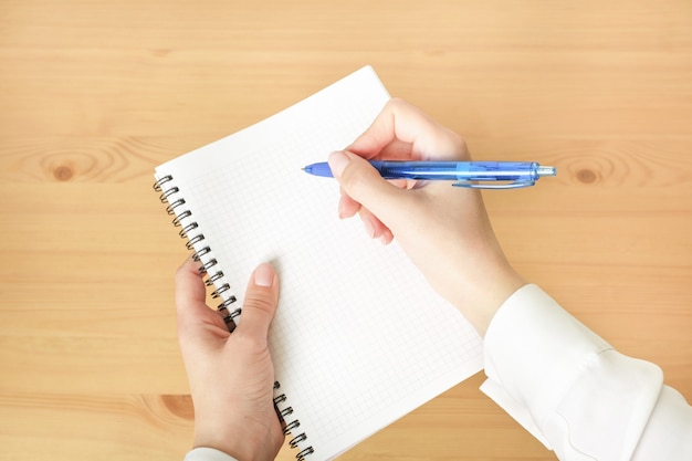 Foto leeres notizbuch und weibliche hand mit stift auf hölzernem schreibtisch.