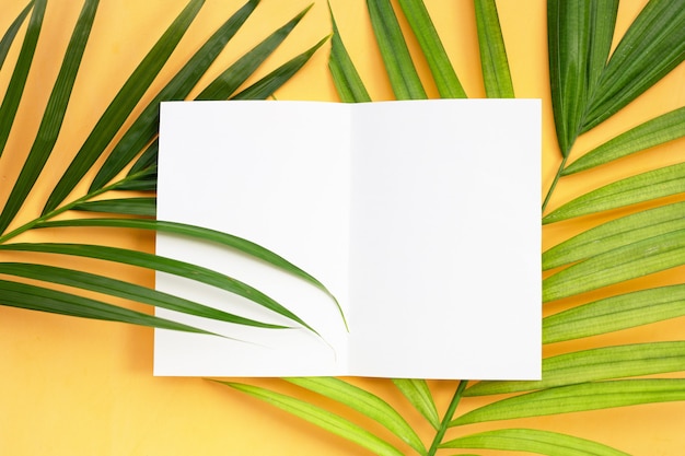 Leeres Papier auf tropischen Palmblättern auf gelbem Hintergrund.