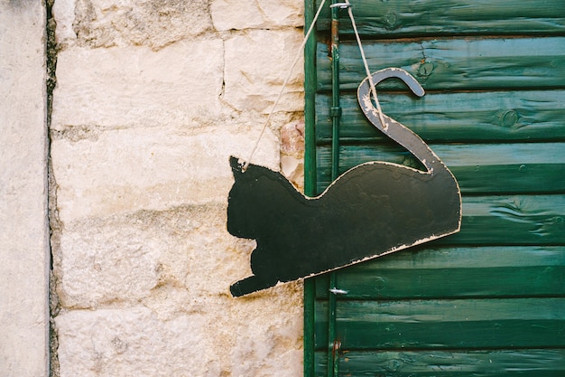 Leeres Schild in Form einer schwarzen Katze, die an einer grünen Holztür hängt