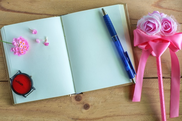 Leeres Tagebuchnotizbuch, rosa Blume, Uhr und Stift auf Holztisch