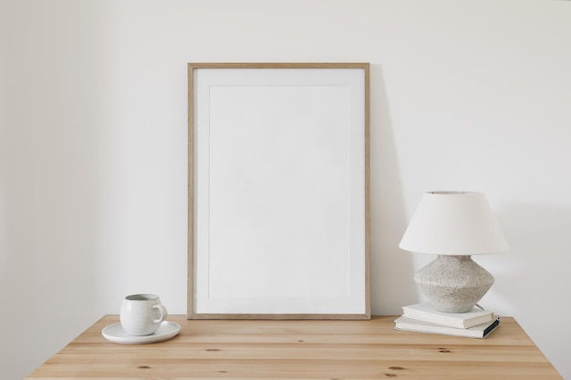 Leeres vertikales Bilderrahmen-Mockup aus Holz Tasse Kaffee auf alten Büchern Leinenschirmlampe auf dem Tisch Weißer Wandhintergrund Home-Office-Konzept Eleganter Arbeitsbereich Skandinavisches Innendesign