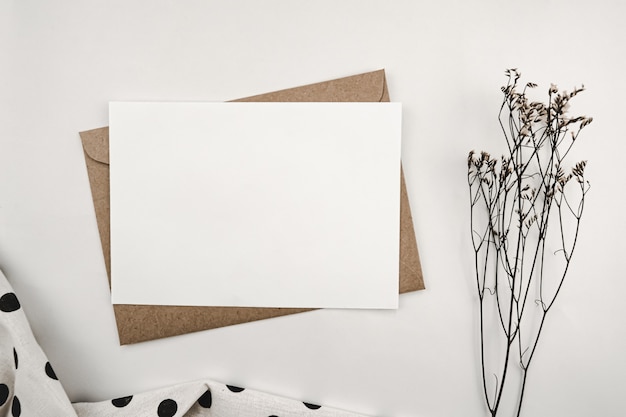 Foto leeres weißes papier auf braunem papierumschlag mit limonium-trockenblume und weißem tuch mit schwarzen punkten