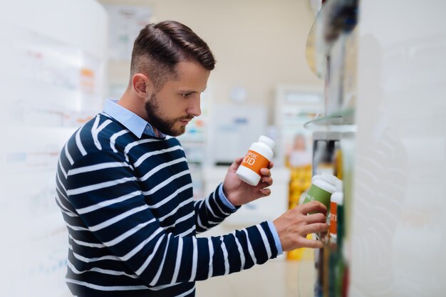 Leg es. Aufmerksame männliche Person, die den Kopf neigt, während sie eine Flasche mit Tabletten nimmt