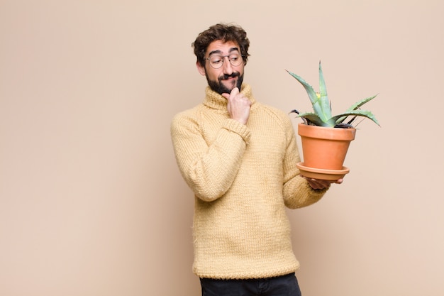 Legal jovem segurando uma planta de cacto contra parede plana