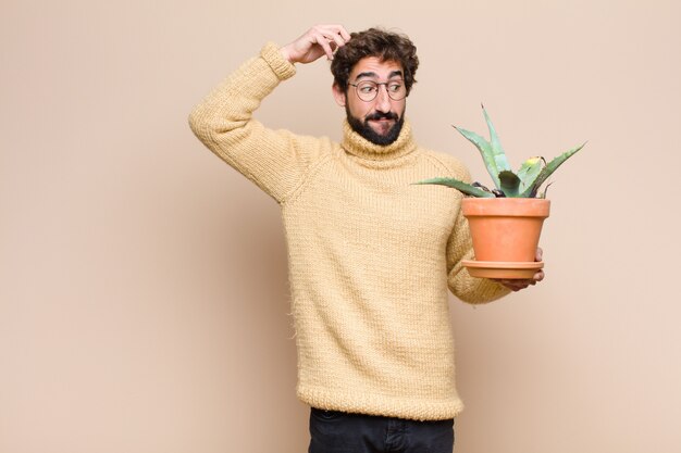 Legal jovem segurando uma planta de cacto contra parede plana