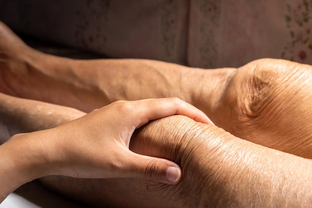 Legen Sie eine junge Hand auf das Bein der älteren Person, um nach Krankheitssymptomen zu suchen, Gesundheitskonzept