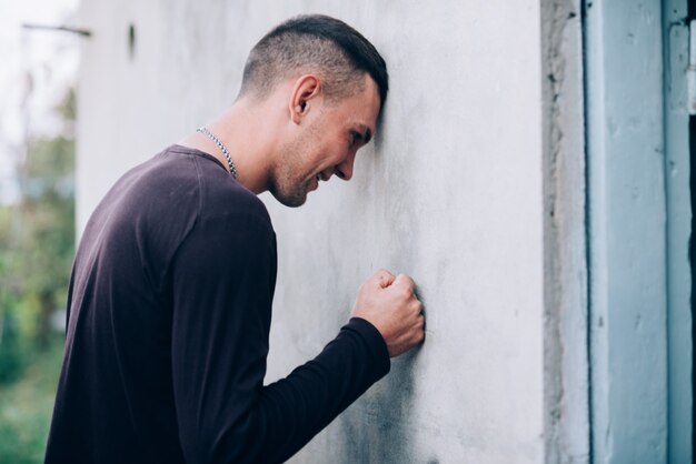 Legen Sie Ihren Kopf gegen die Wand, Nahaufnahme eines Mannes in Depressionen und Frustration