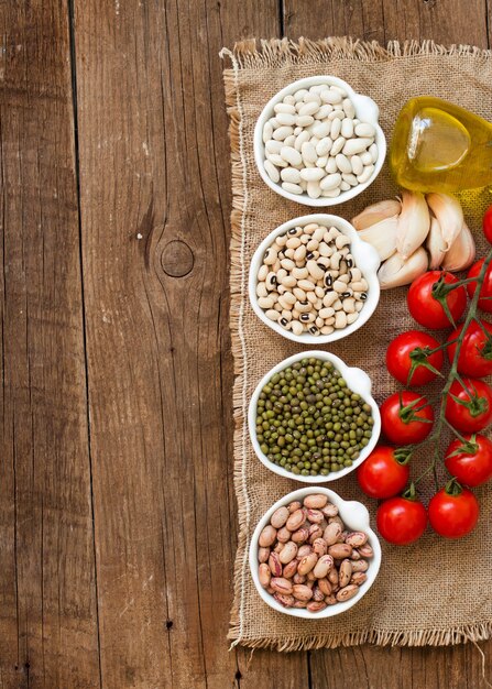 Legumbres en cuencos, tomates, ajo y aceite de oliva en la vista superior de la mesa de madera con espacio de copia