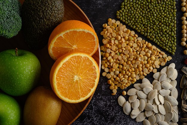 Foto legumbres con naranja cortada a la mitad kivi y manzana en un fondo de suelo de cemento negro