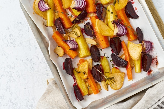 Legumes assados coloridos na bandeja com pergaminho. Mistura de cenouras, beterrabas, nabos, rutabaga, cebola