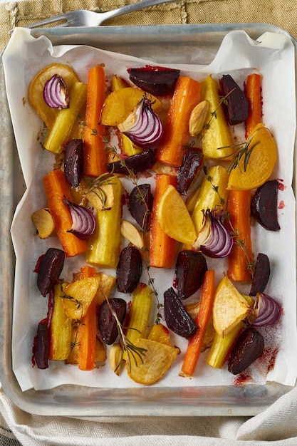 Legumes assados coloridos na bandeja com pergaminho. Mistura de cenouras, beterrabas, nabos, rutabaga