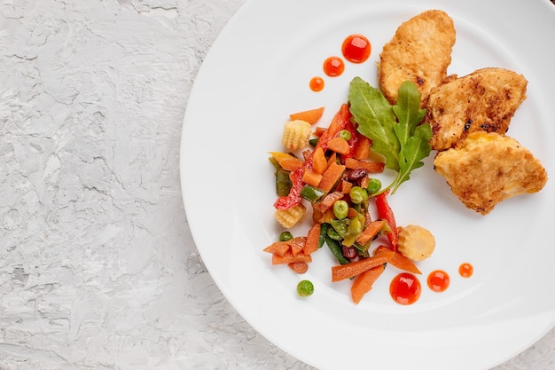 Legumes cozidos com ervas e bifes de frango na massa em um prato branco com gotas de ketchup em um fundo cinza de concreto vista de cima do menu de comida com um lugar para copiar o texto