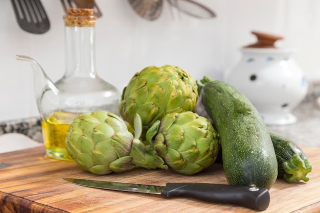 Legumes crus na mesa da cozinha ao lado deles uma panela de óleo se preparando para cozinhar faca em primeiro plano