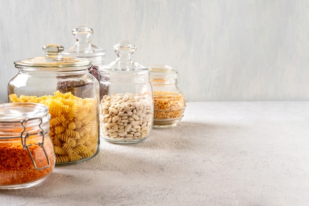 Legumes diferentes em potes de vidro: grão de bico, macarrão, feijão, ervilha, lentilha. Armazenamento de resíduos zero, sem plástico.