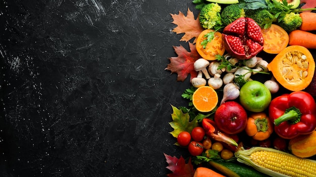 Legumes e frutas de outono em um fundo de pedra preta Abóbora tomates milho romã maçã caqui Vista superior Espaço para cópia grátis