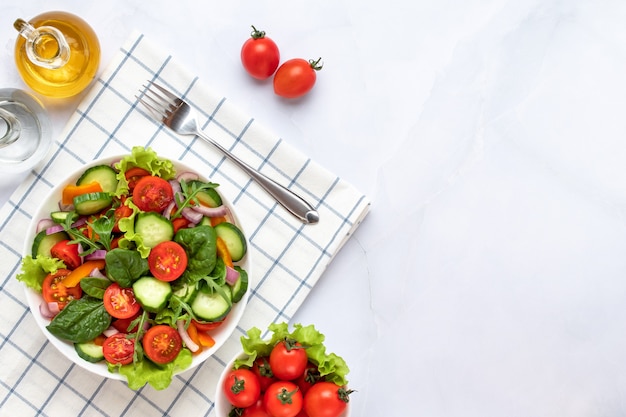 Legumes em um prato branco sobre um fundo de mármore cinza. Vista do topo. Salada feita com tomate cereja, pepino, rúcula, manjericão e temperada com azeite. Conceito de comida saudável, uma dieta vegana. Copie o espaço