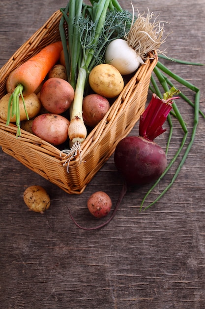 Legumes em uma cesta: beterraba, cebola, alho, endro, batatas, cenouras em um fundo de madeira velha