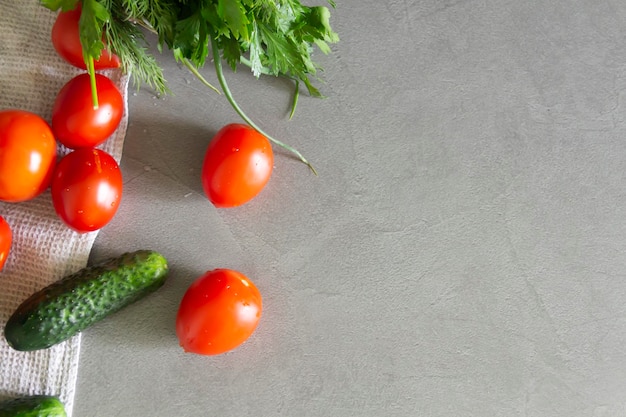 Legumes frescos pepinos tomates e verduras com endro e salsa estão na superfície cinzenta da cozinha em uma toalha de linho