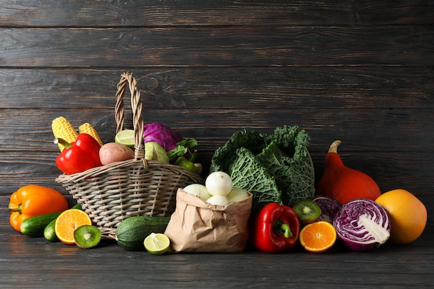 Legumes, frutas, cesta de vime e saco de papel na madeira