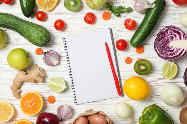 Legumes, frutas e caderno com caneta na vista superior de madeira