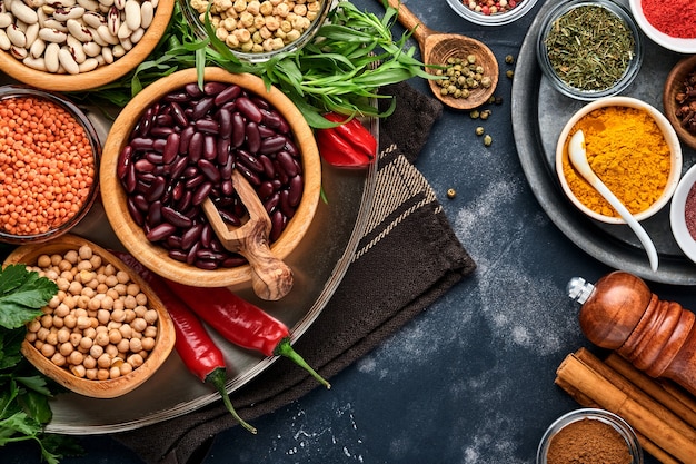 Legumes, lentilhas, grão de bico, feijão sortido, saborosa mercearia de especiarias ingredientes apetitosos para cozinhar uma cozinha saudável na mesa preta. dieta da perda de peso e luta contra o conceito de colesterol. vista do topo.