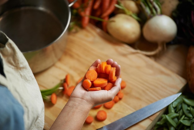 Legumes mãos e pessoa com cenoura e tábua de madeira para cozinhar almoço e nutrição dieta em casa bem-estar saúde e alimentos orgânicos com refeição vegetariana e ingredientes para salada em uma cozinha