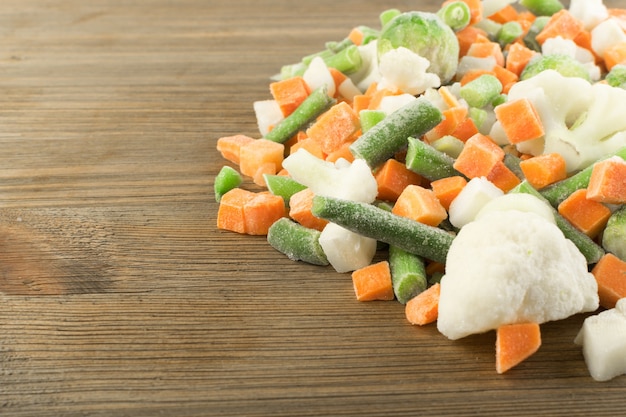 Legumes mistos congelados na mesa de madeira. Cenoura picada crua, couve-flor, cebola, feijão verde e couve de Bruxelas