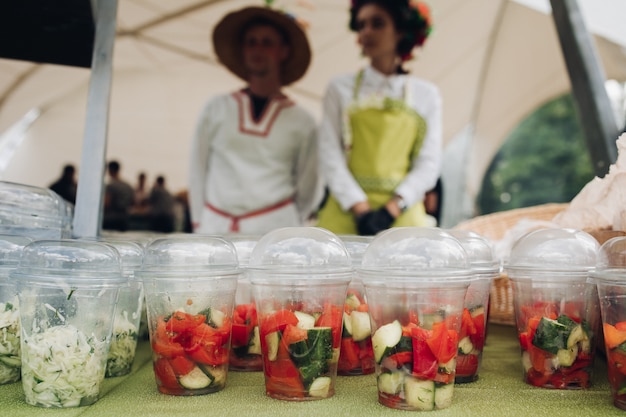 Legumes orgânicos em copos para ir. close-up de um monte de copos de plástico cheios de legumes picados e saladas em cima da mesa no festivel comida. salada para viagem e legumes em cima da mesa.