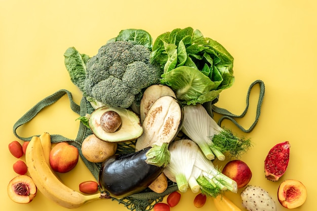 Legumes verdes frescos e frutas em um saco de corda verde em um fundo amarelo