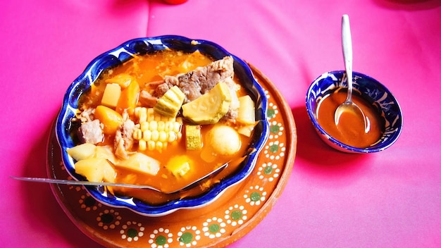 Foto lehmplatte mit pozole, traditionelles mexikanisches essen, rosa tischdecken, metalllöffel