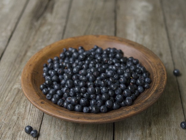 Lehmschüssel mit Blaubeeren auf einem alten Holztisch.