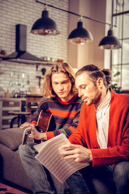 Lehrender Student. Bärtiger professioneller talentierter Musiklehrer mit roter Strickjacke, der seinen Schüler unterrichtet