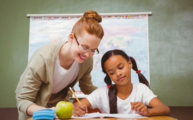 Foto lehrer, der kleines mädchen mit hausarbeit im klassenzimmer unterstützt