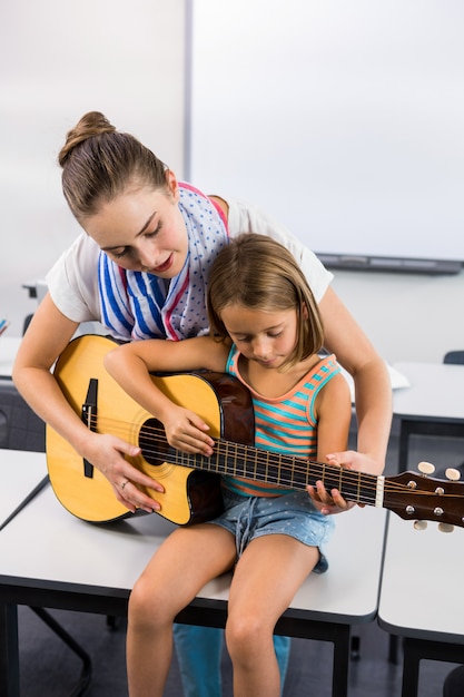 Lehrer, der Mädchen hilft, Gitarre im Klassenzimmer zu spielen