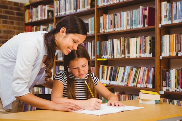 Lehrer, der Mädchen mit Hausarbeit in der Bibliothek unterstützt