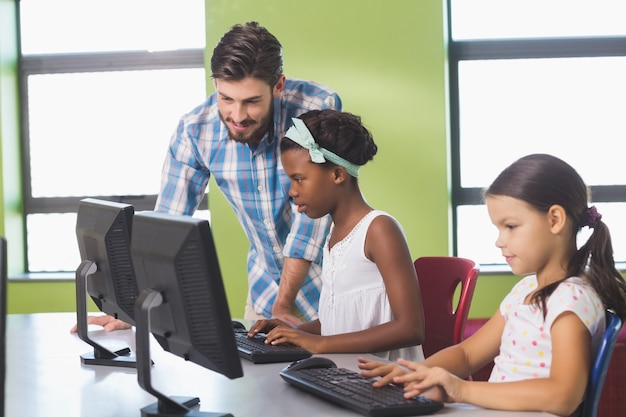 Lehrer, der Schulmädchen beim Lernen des Computers unterstützt