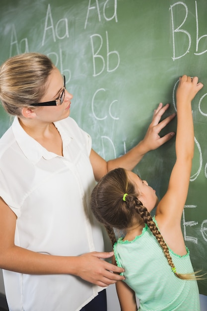 Lehrer, der Schulmädchen hilft, Alphabet an der Tafel im Klassenzimmer zu lernen