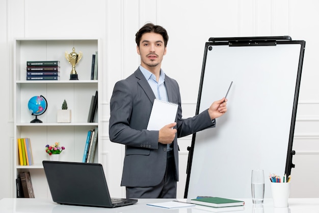 Lehrer junger Ausbilder im Büroanzug in der Klasse mit Computer am Whiteboard