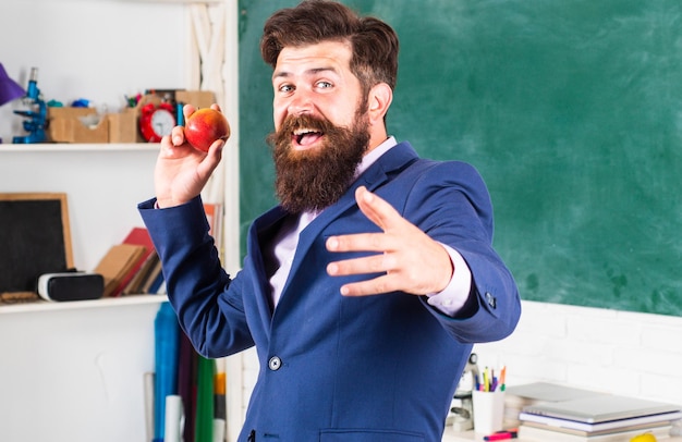 Lehrer mit einem Apfel. Aufgeregter Mannprofessor, der formellen Anzug mit lustigem Gesicht der lustigen Ausdrucksgefühle trägt.