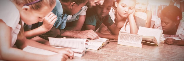 Foto lehrer und kinder liegen auf dem boden und lesen ein buch in der bibliothek