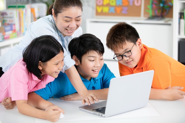 Lehrer und nette asiatische Kinder, die zusammen Laptop-Computer verwenden.