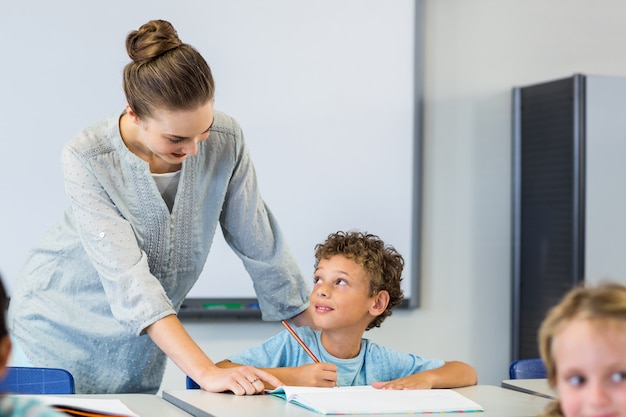 Lehrerin beim Betrachten des Schülers, der auf Buch schreibt