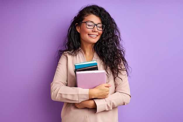 Lehrerin mit Büchern in den Händen lokalisiert auf lila Wand, junge Dame in Brillen genießen Bildung, lachen