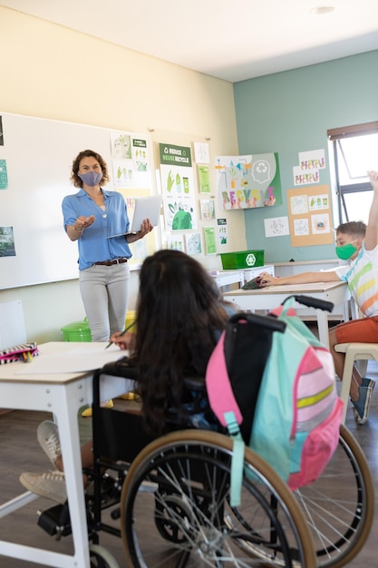 Lehrerin mit Gesichtsmaske und Laptop, um Schüler im Unterricht zu unterrichten