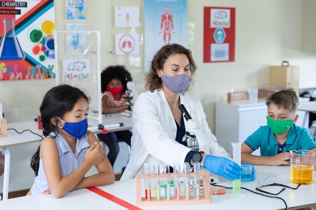 Lehrerin mit Gesichtsmaske und Schutzbrille unterrichtet Schüler im Labor