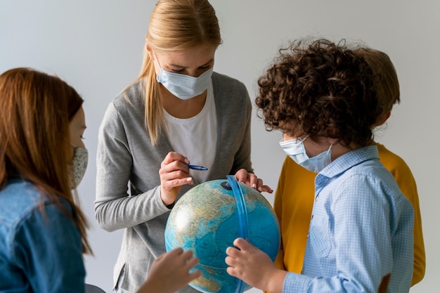 Foto lehrerin mit medizinischer maske, die geographie mit globus in der klasse unterrichtet