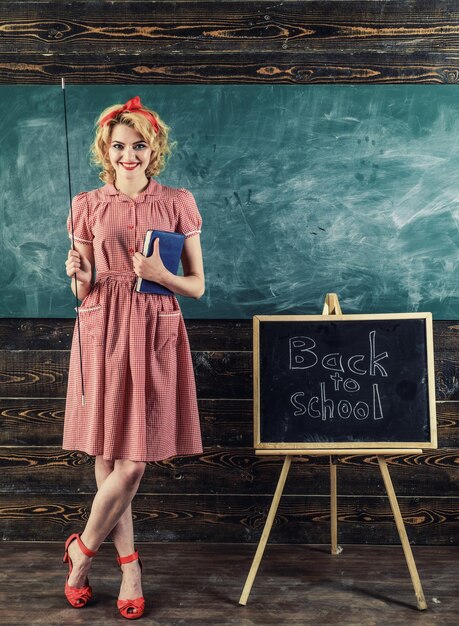 Lehrerlächeln mit Buch und Zeiger im Klassenzimmer. Glücklicher Lehrer zurück zu Schule über Tafelhintergrund. Hübsch und genial