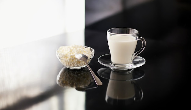 Leichtes Frühstück mit Milchprodukten Ein Glas Milch und eine Tasse mit Hüttenkäse auf schwarzem Glanz