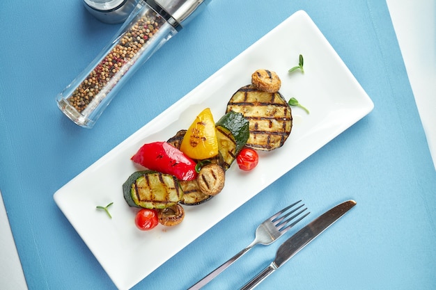 Leichtes und diätetisches Grillgemüse, Paprika, Zucchini, Pilze in einem weißen Teller auf blauer Tischdecke.